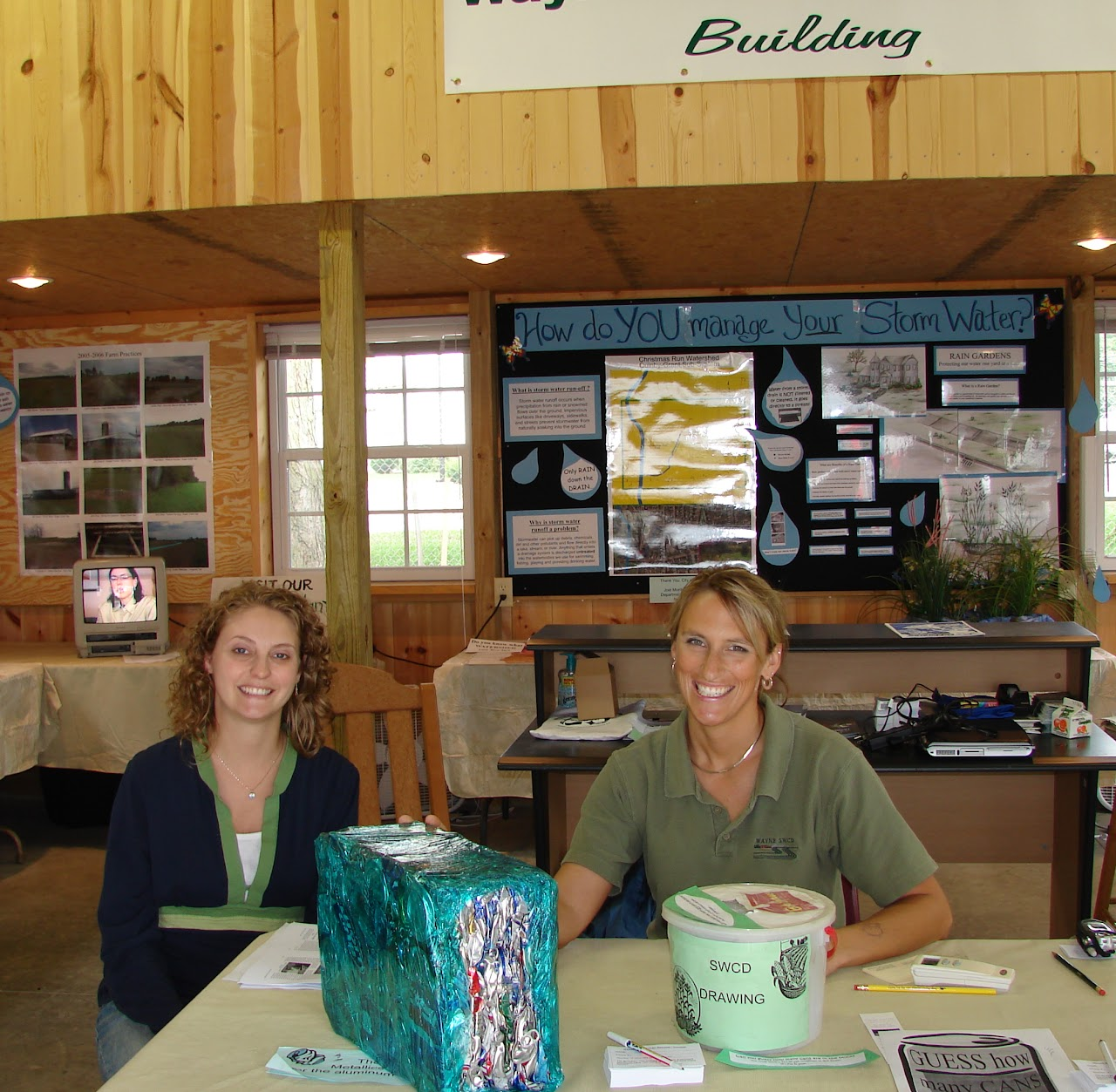 Two people at a booth about stormwater management, with informational displays and a donation box on the table.