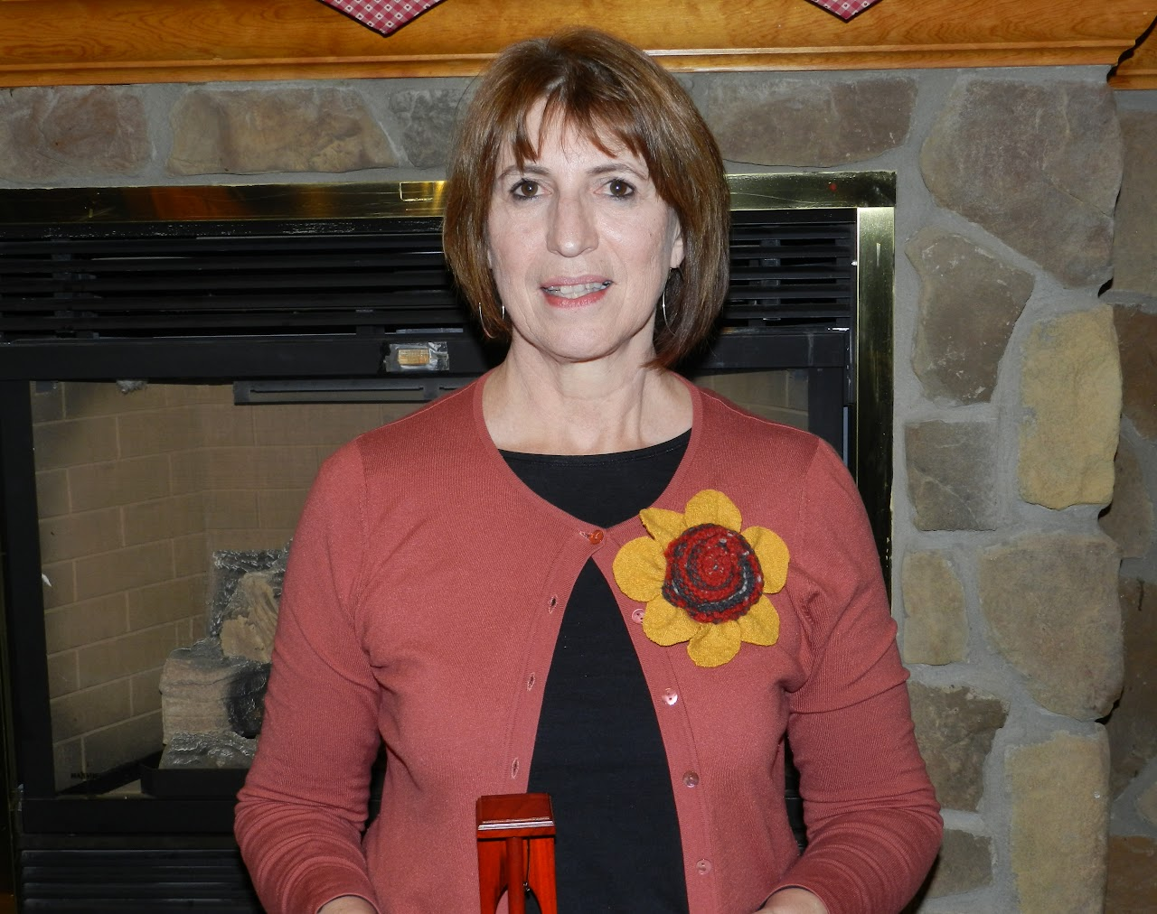 A person wearing a pink cardigan with a large flower decoration, standing in front of a stone fireplace.