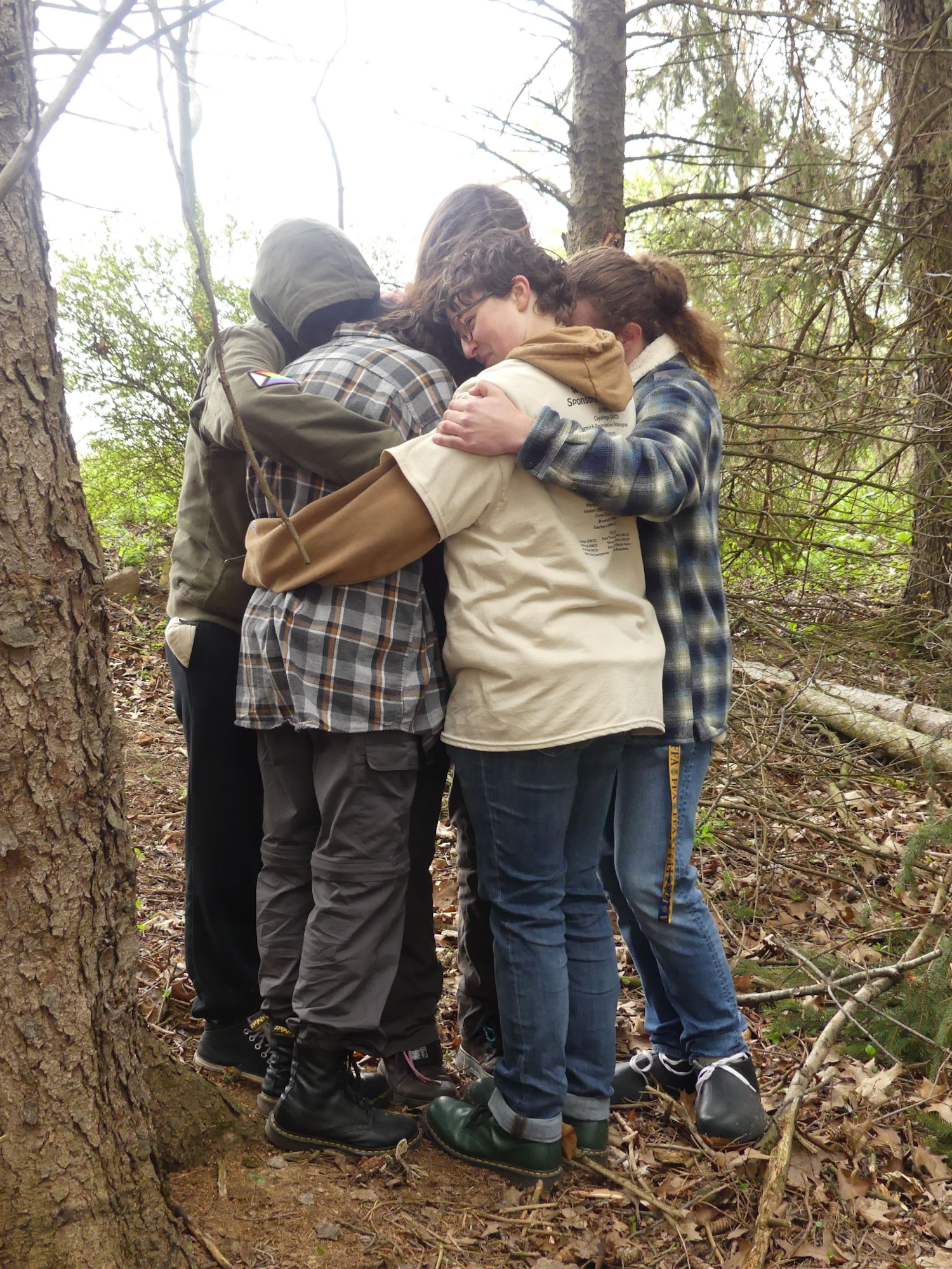 A group of people hugging in a forest clearing, surrounded by trees.