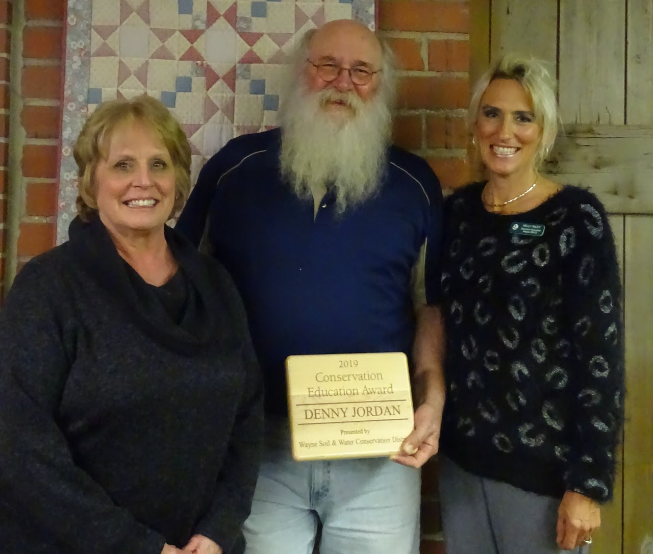 Three people smiling; the person in the middle holds a 2019 Conservation Education Award.