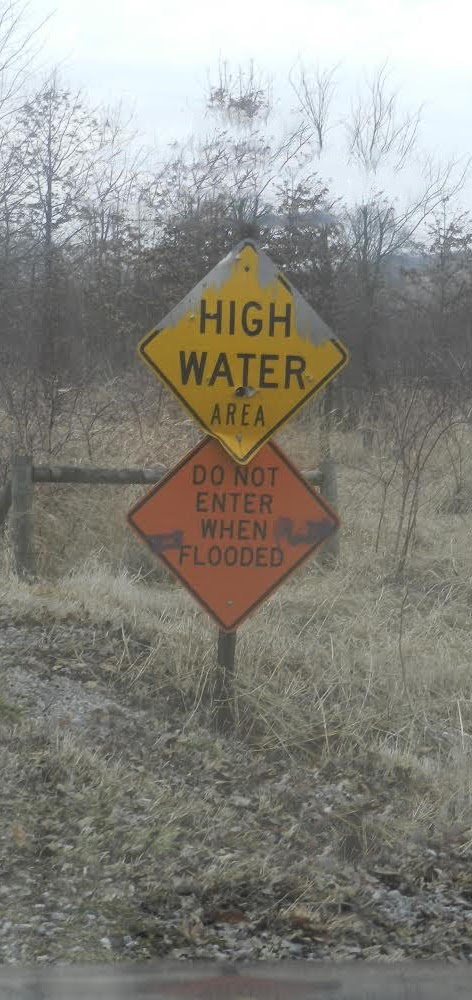 Two warning signs: "High Water Area" and "Do Not Enter When Flooded" on a rural road.