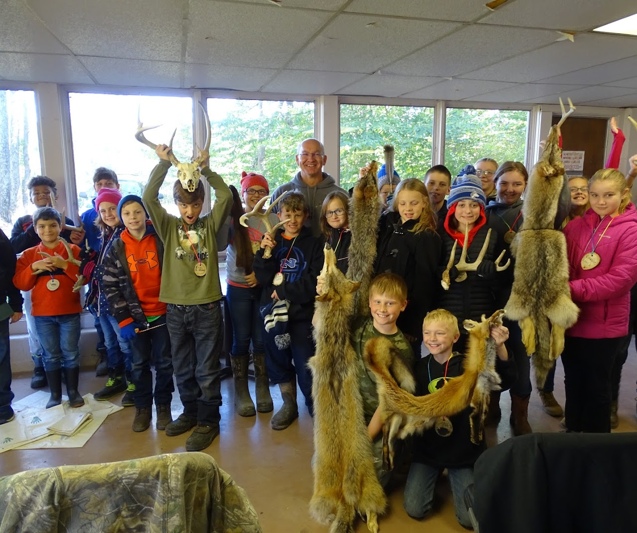 A group of kids and an adult indoors holding animal pelts and antlers, smiling at the camera.
