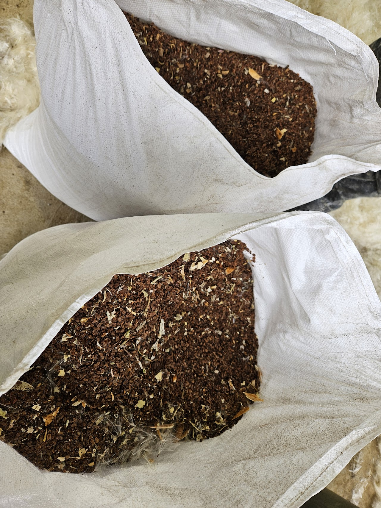 Two white sacks filled with brown, coarse material resembling mulch or feed.