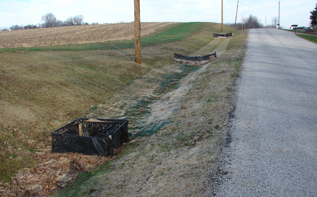 Gravel road with drainage ditches and erosion control silt fences in a rural area.