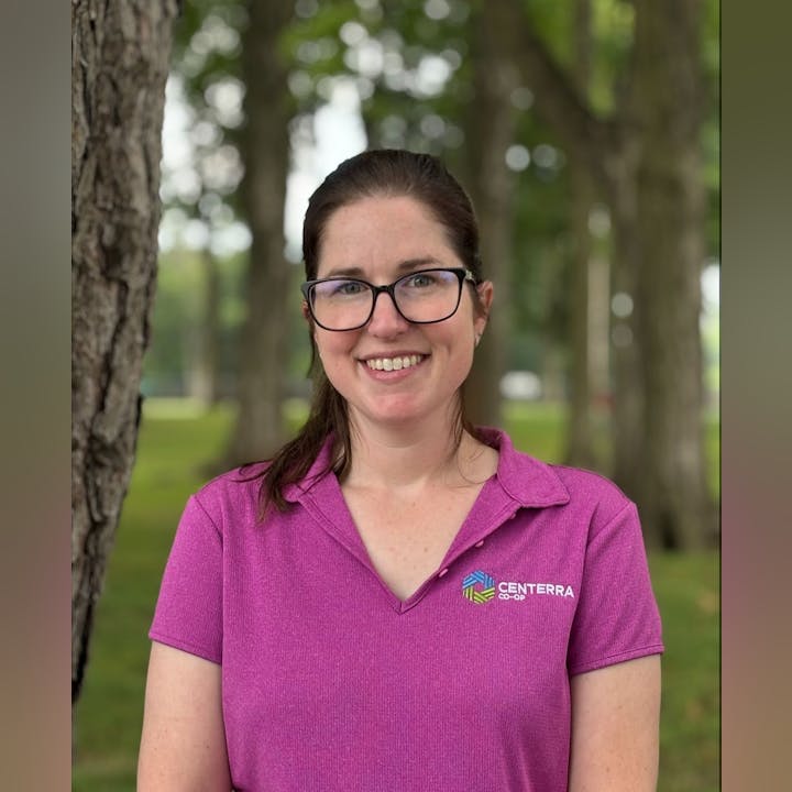 A person with glasses, wearing a purple "Centerrra Co-op" shirt, stands outdoors near trees.