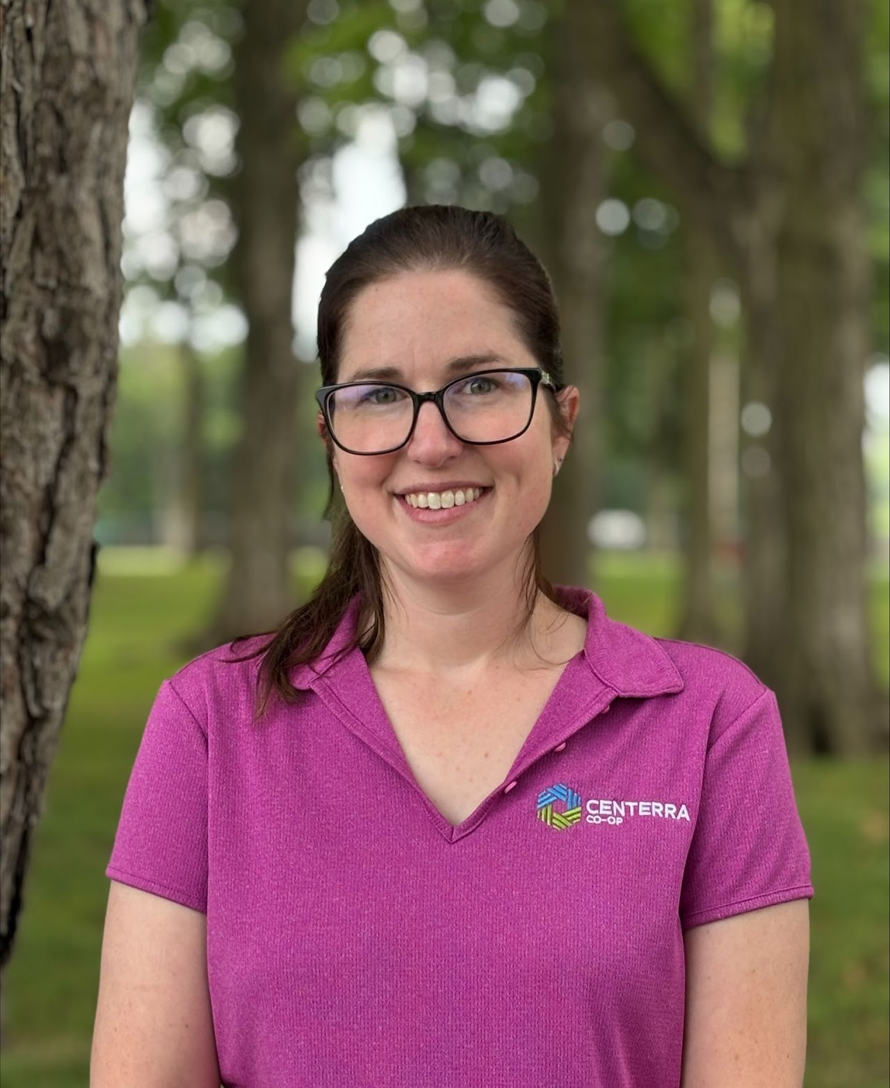 A person with glasses, wearing a purple "Centerrra Co-op" shirt, stands outdoors near trees.