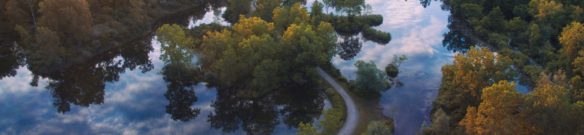 Aerial view of a winding path through a forested area with trees reflected in a calm river.