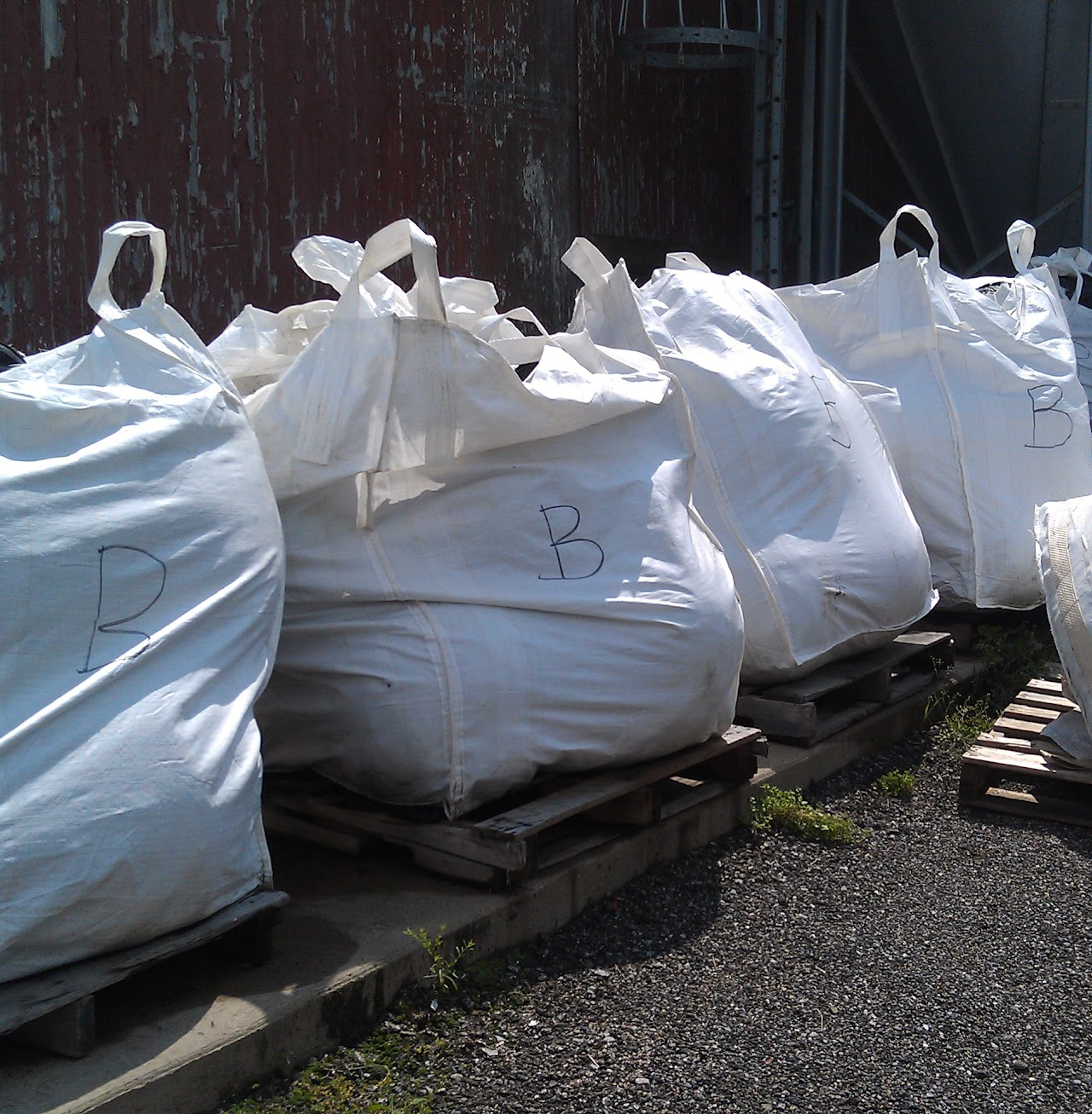 Large white bags with the letter "B" on pallets outside a building.