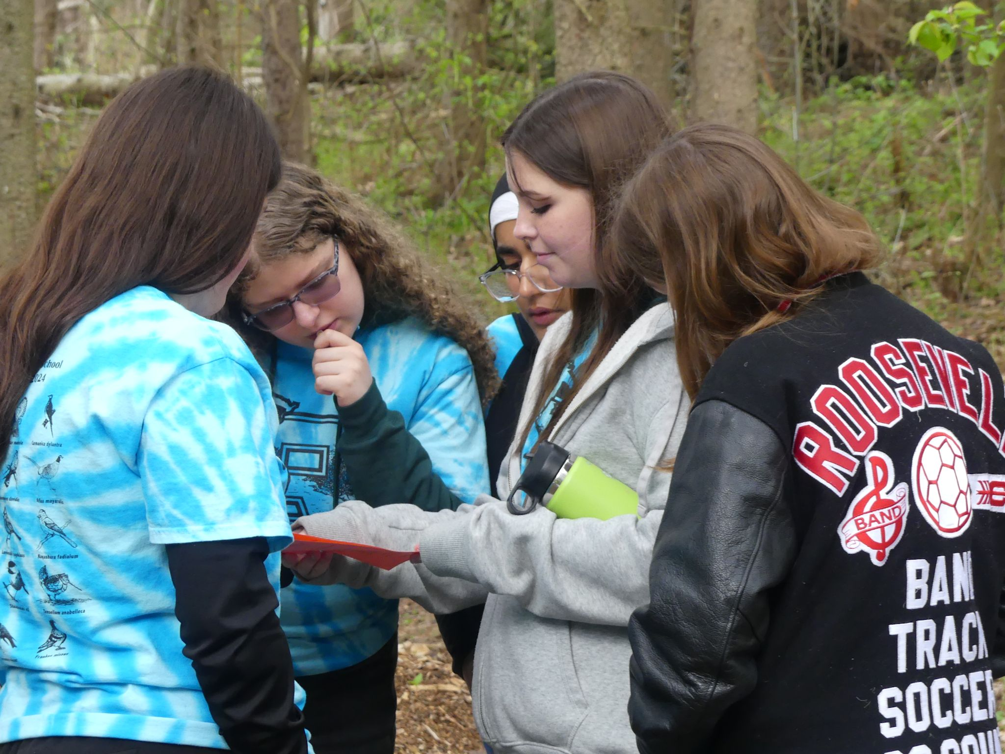 A group of people outdoors, wearing blue and black jackets, looking at a piece of paper.