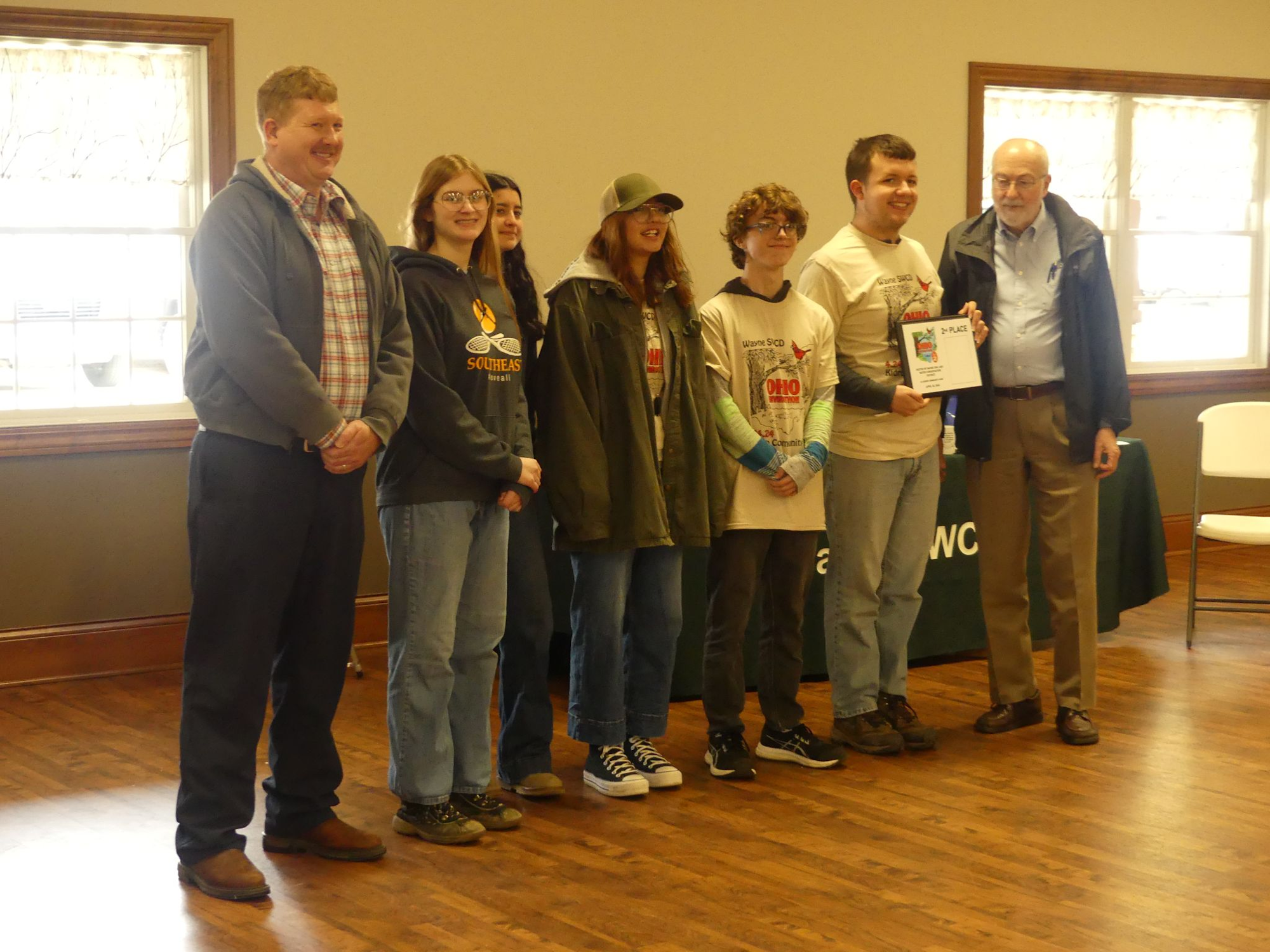 A group of people standing indoors, one holding a plaque, possibly a recognition or award event.