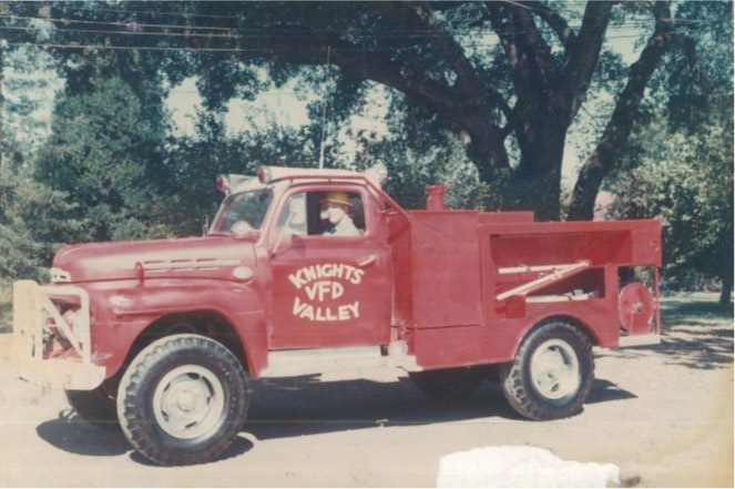 A vintage red fire truck labeled "KNIGHTS VALLEY VFD" parked on a sunny street with trees in the background.
