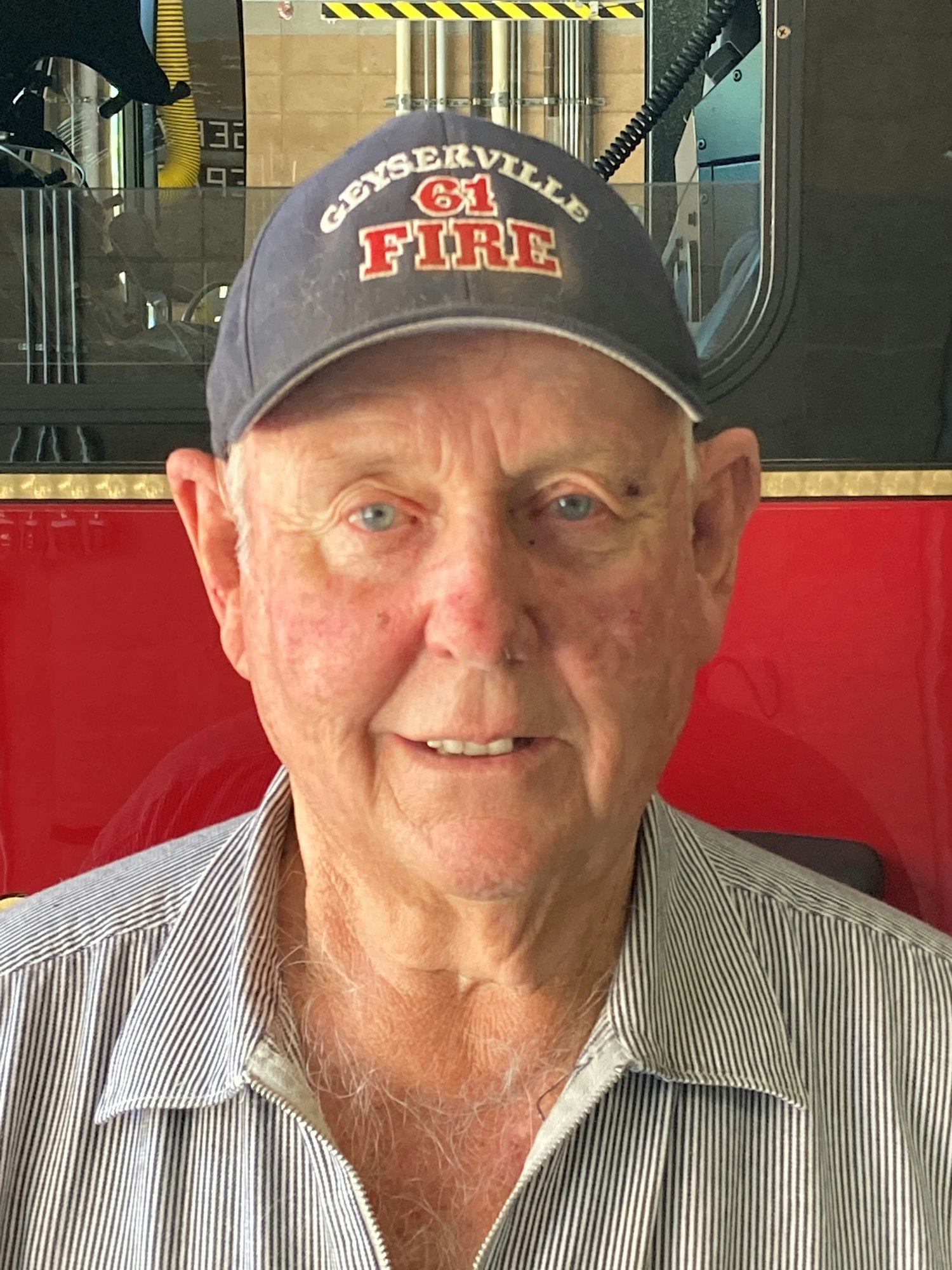 An older man wearing a cap that says "Ceresville Fire" is smiling, with a fire station background visible.