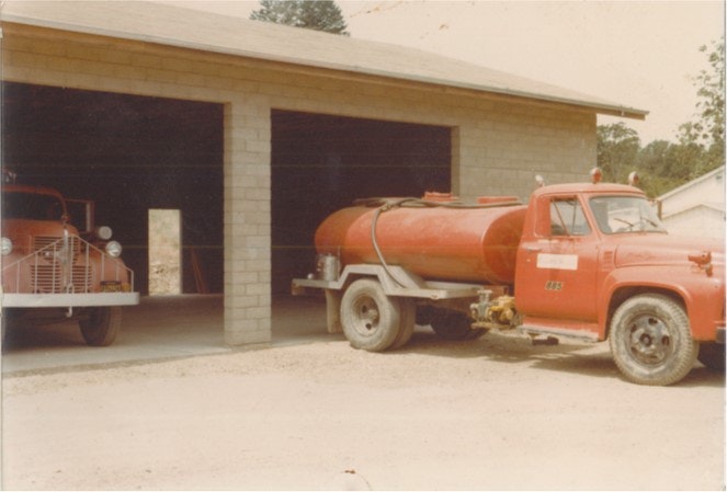 Two red fire trucks parked outside and inside a garage.
