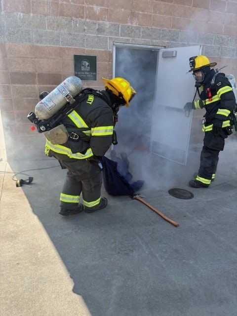 Firefighters in gear handling a smoke-filled situation outside a building.