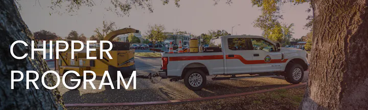 A truck and wood chipper for a community chipper program, with trees and a parking area in the background.