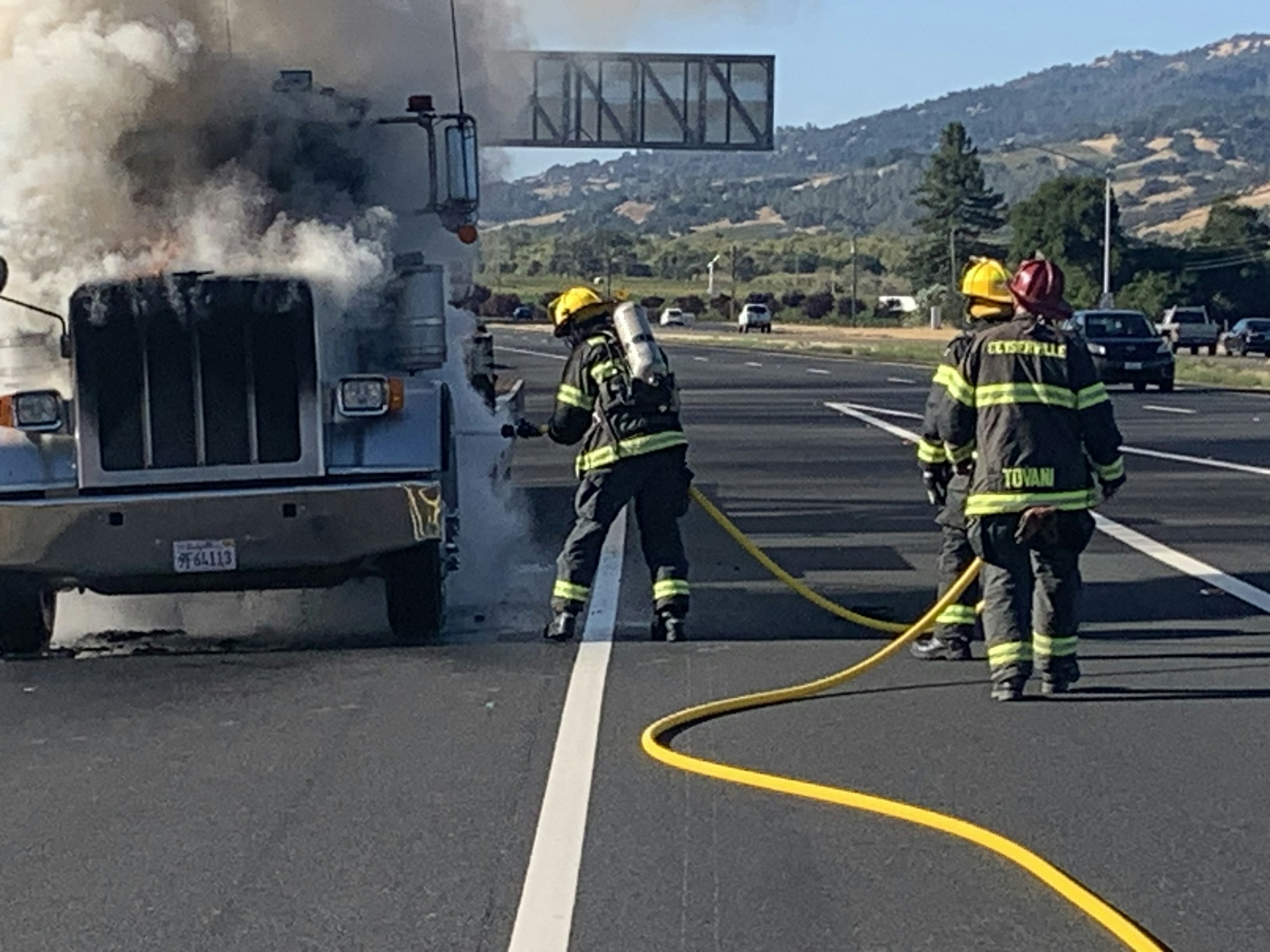 Firefighters extinguishing a smoking vehicle on a highway.