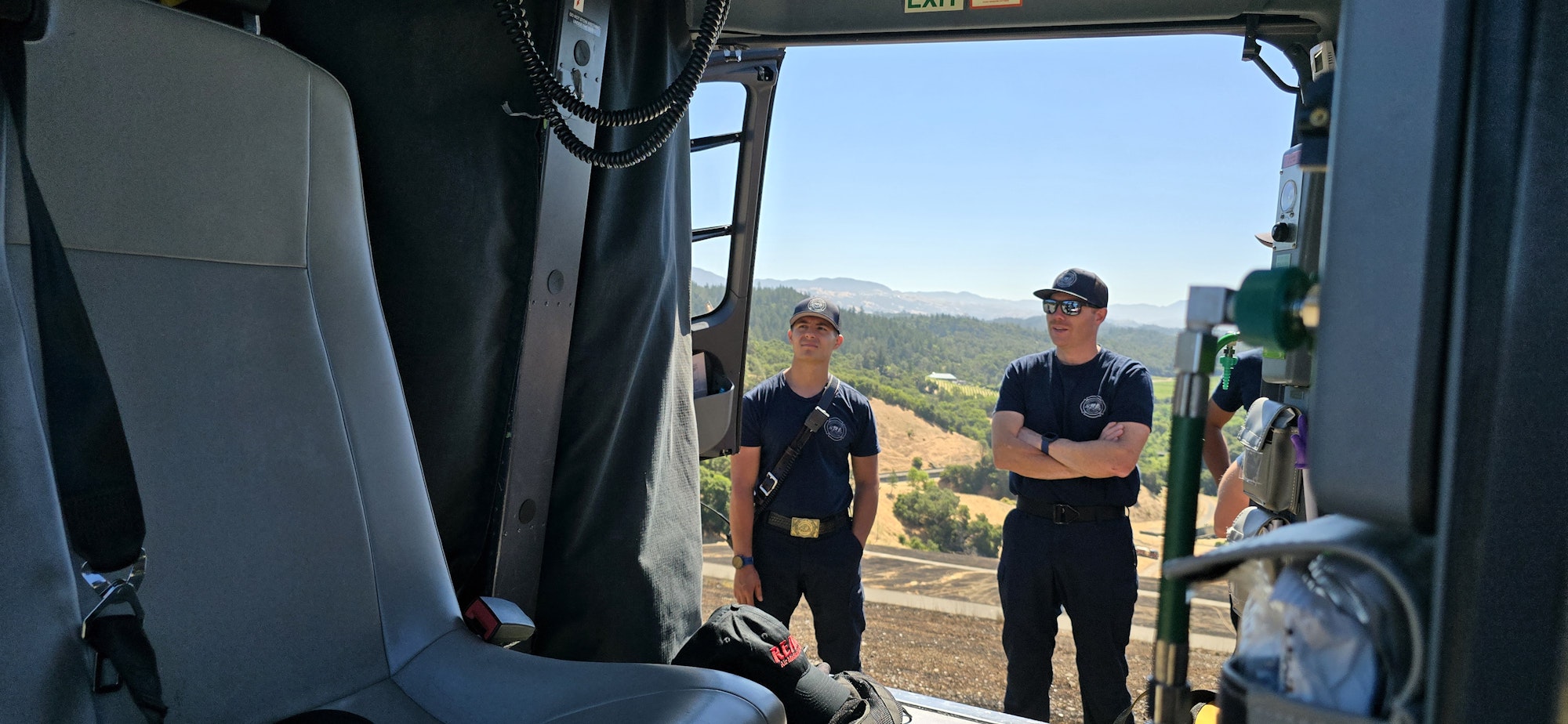 Two firefighters standing outside a helicopter looking into the helicopter interior.