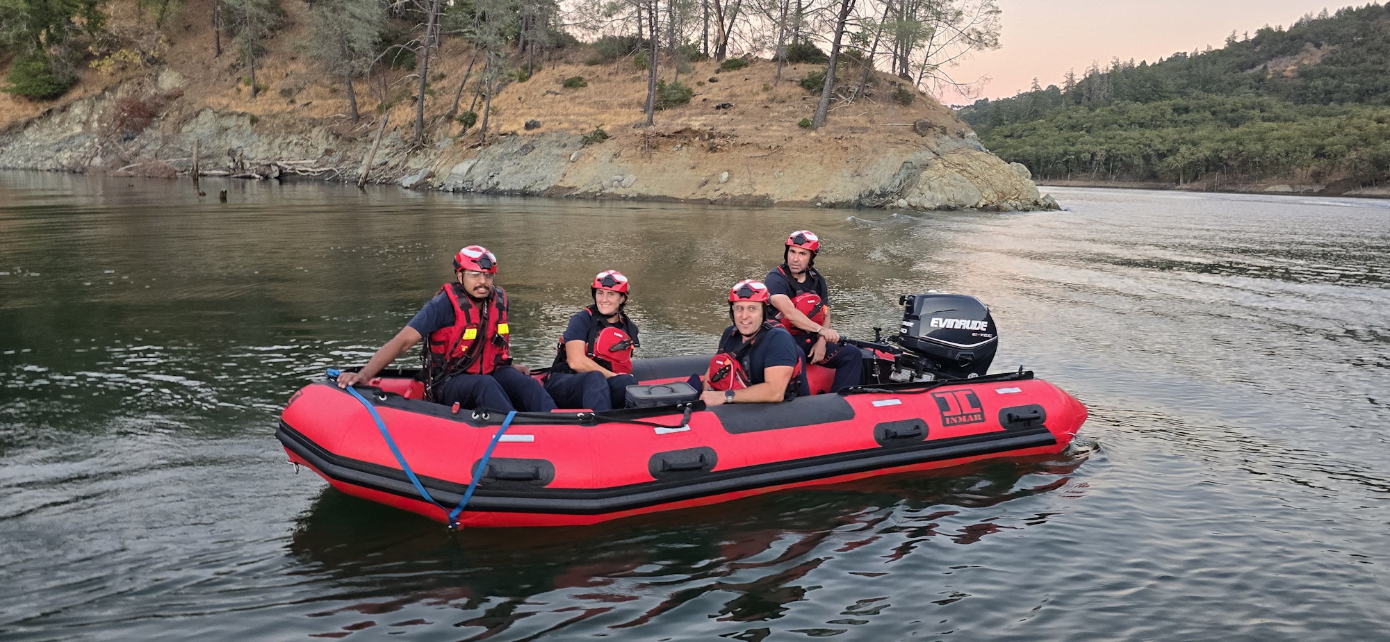 Four rescue personnel wearing helmets and life jackets on an inflatable boat on a river.