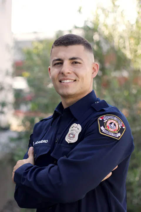 A firefighter in uniform, smiling with arms crossed, with a blurred background.