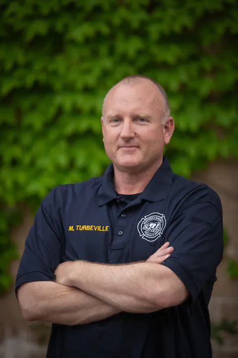 Adult, male, wearing blue polo shirt with arms crossed