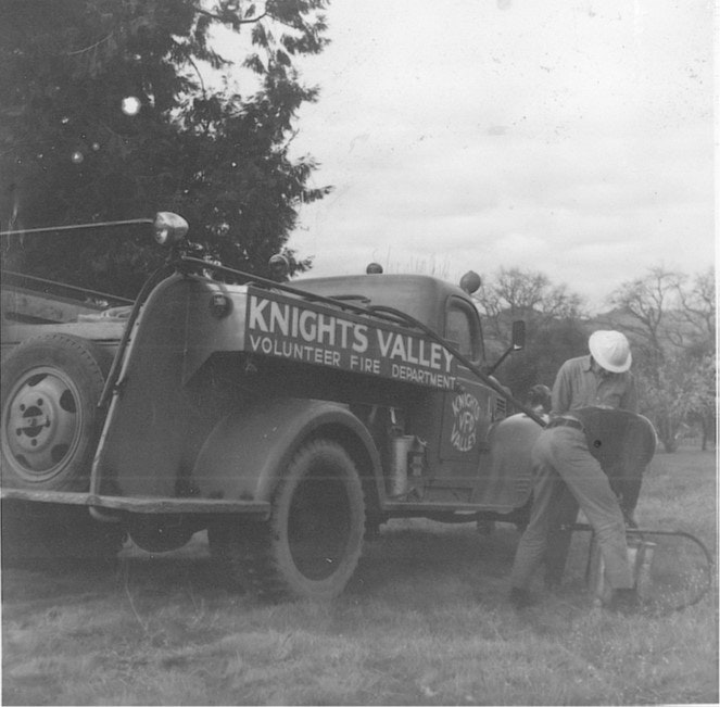 A vintage Knights Valley Volunteer Fire Department truck with two people working beside it.