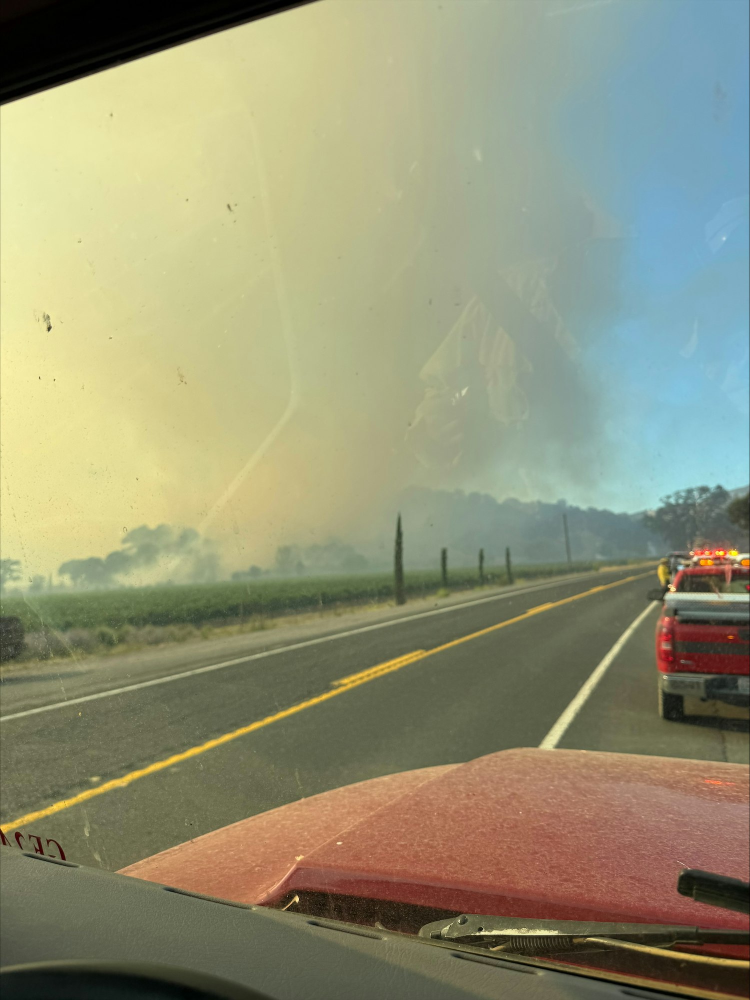 The image shows a view from a vehicle with a foggy background, likely smoke from a fire, and emergency vehicles on the roadside.