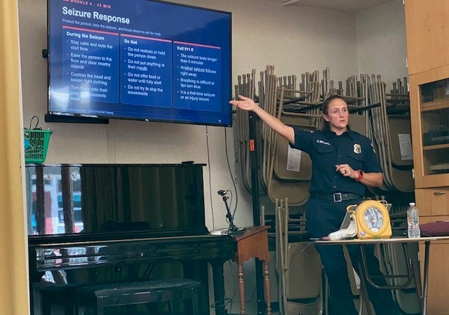 A woman in a uniform is giving a presentation on seizure response, with guidelines displayed on a screen.