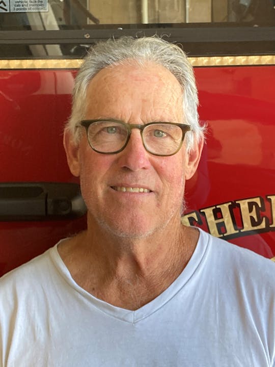 A smiling man with glasses against a red backdrop.