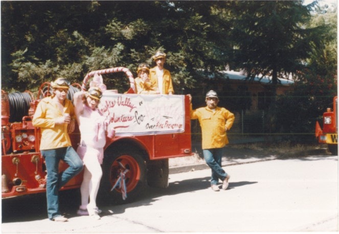People in costumes stand with a fire truck labeled "Valley Volunteer Co." in an outdoor setting.