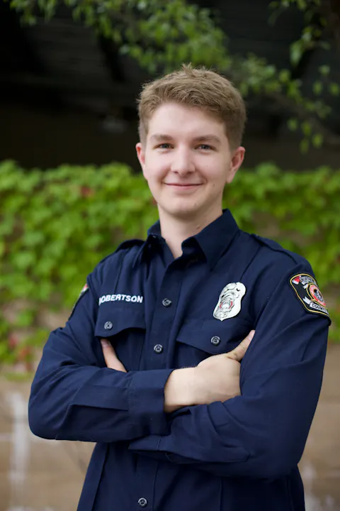 A person in a uniform, arms crossed, smiling, with a name tag and badges on the shirt.
