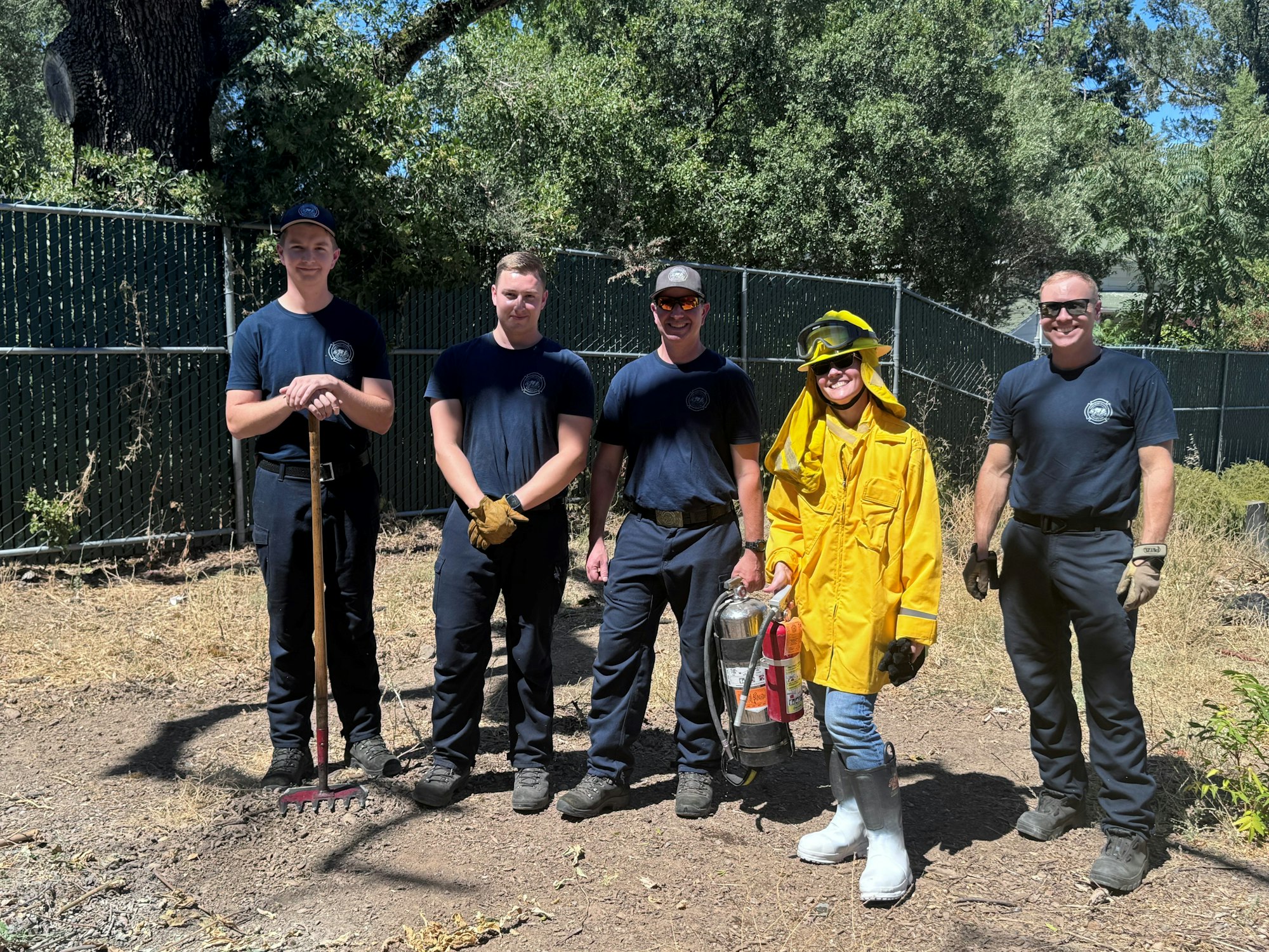 Five individuals dressed in firefighting gear, one in yellow, standing outdoors.