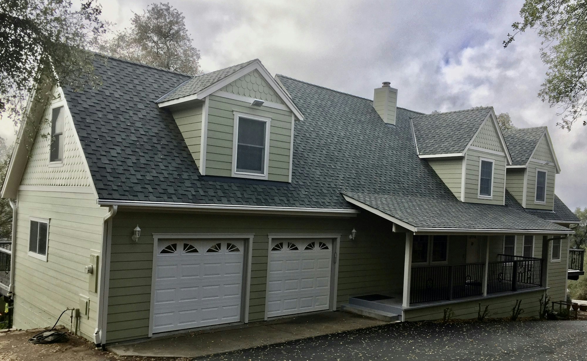 A two-story house with a double garage and a porch, surrounded by trees.