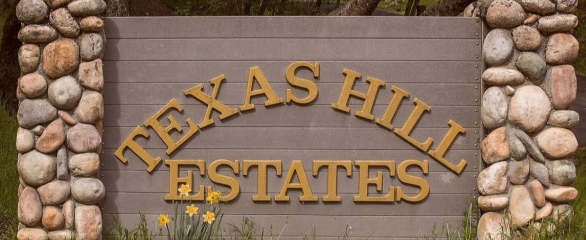 A stone sign reading "Texas Hill Estates" with daffodils at the base.