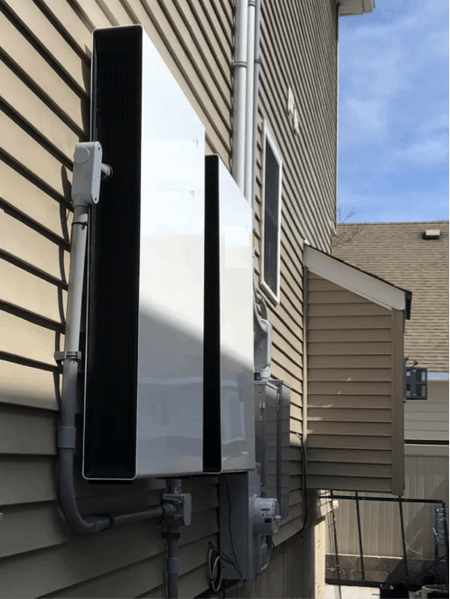 Outdoor HVAC unit mounted on a siding-clad wall with pipes and wiring.