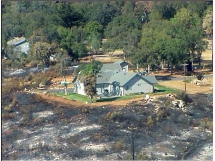 House surrounded by scorched earth, standing intact after a wildfire.