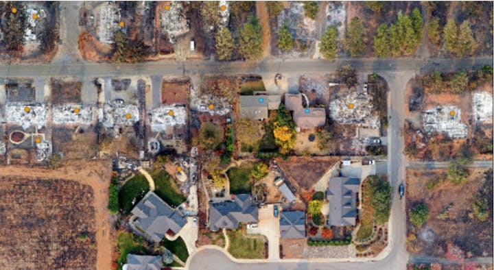 Aerial view of a neighborhood with burnt houses next to intact ones, highlighting the devastating selectivity of a wildfire.