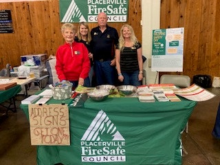A group of four people at a booth for the Placerville FireSafe Council, promoting address signs and fire safety resources.