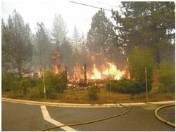 A building on fire with smoke, surrounded by trees, viewed from across a street.