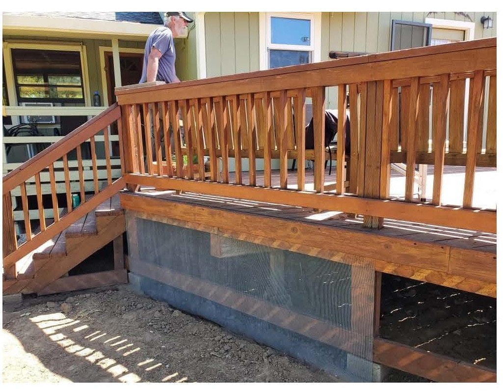 Wooden deck with a railing, person walking on it, and a house in the background.