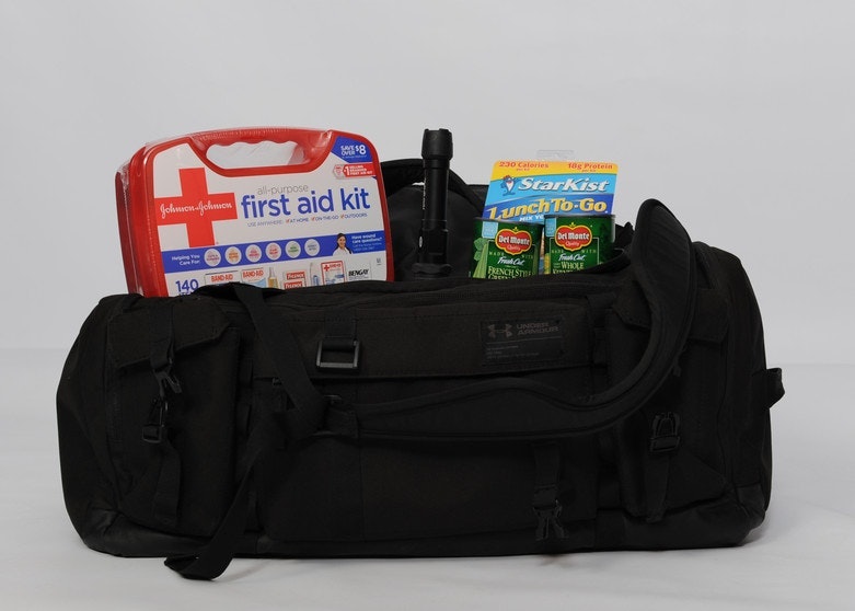 A first aid kit, canned food, and a flashlight on a black duffel bag.