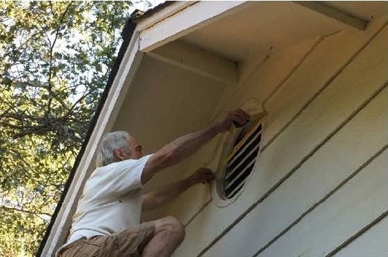 A person adjusting a vent on the side of a house, under the eaves.