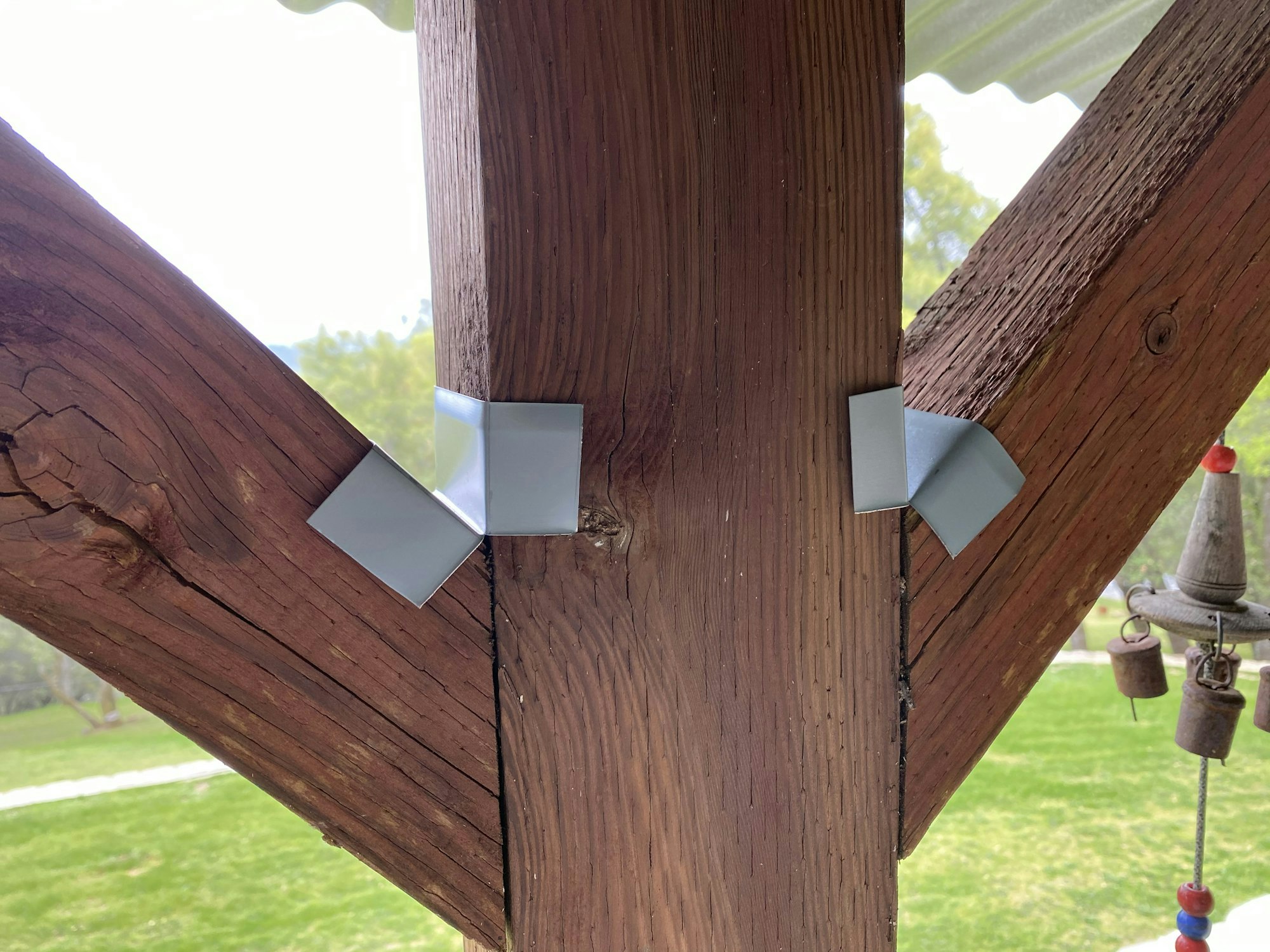 Wooden post with metal brackets and a glimpse of a wind chime.