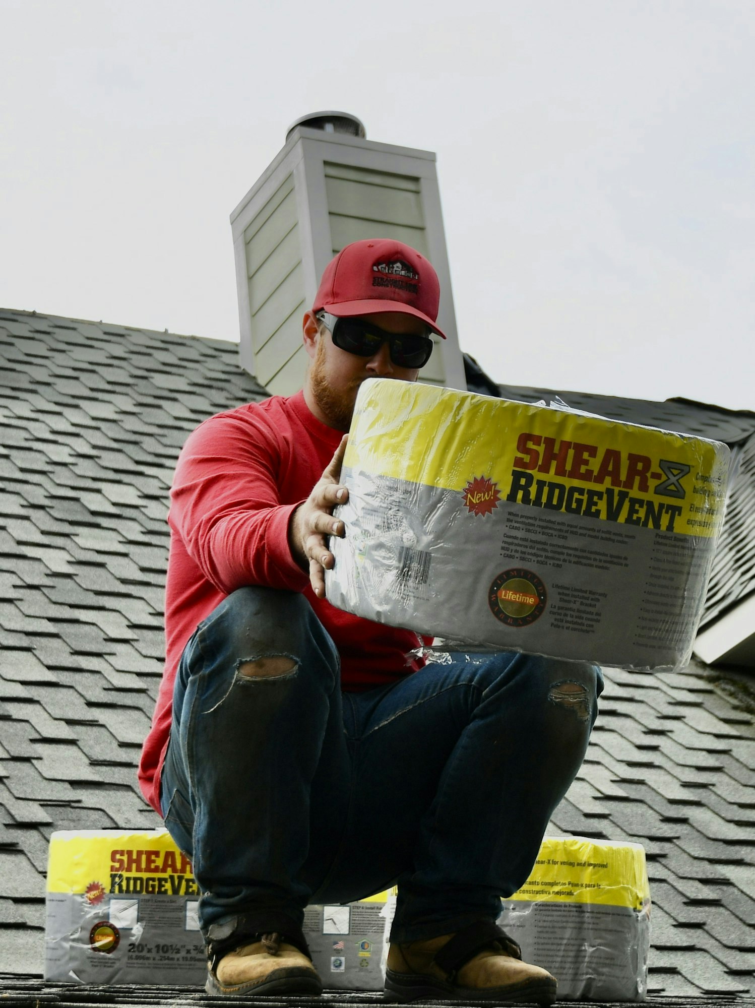 Man in red shirt on roof holding construction material.