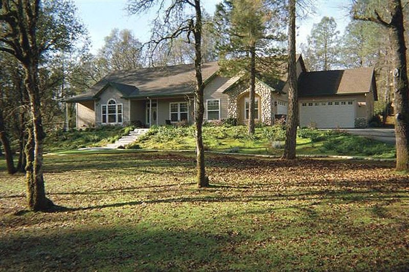 A single-story house with a garage, front porch, surrounded by trees, and a lawn covered with fallen leaves.