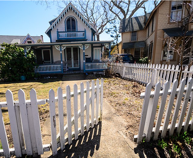 Victorian-style house with a white picket fence and clear blue sky.