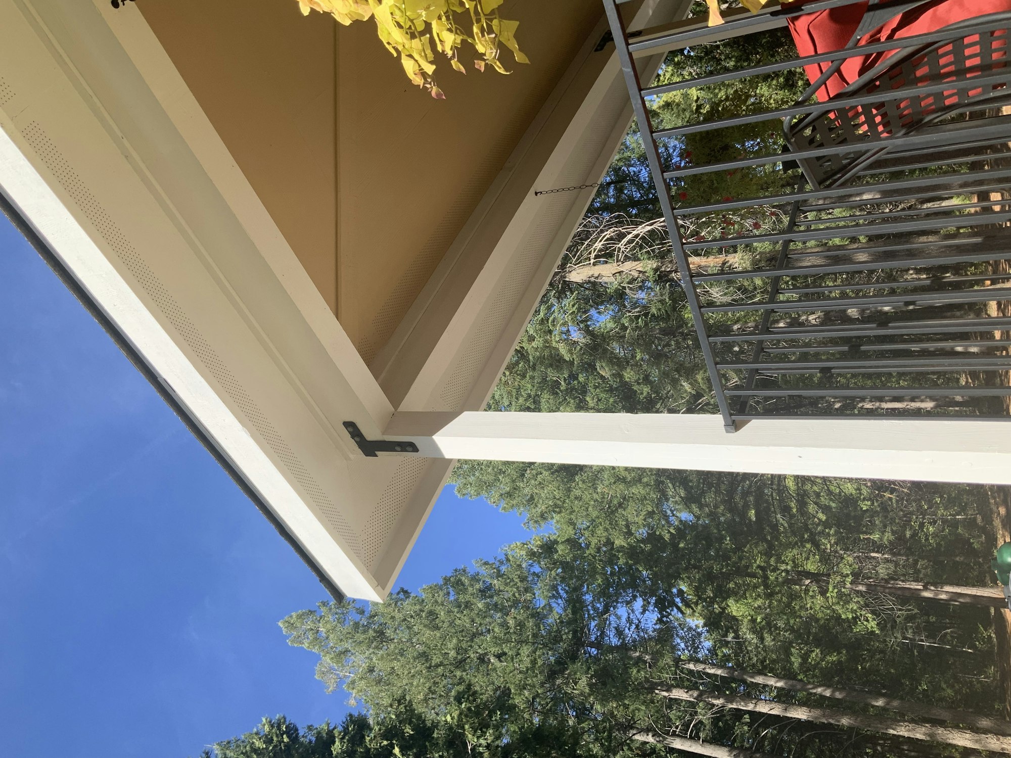 A house corner with a porch railing looking towards a blue sky and trees.