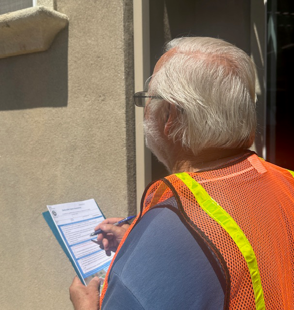 Person in an orange safety vest writing on a form in sunlight.