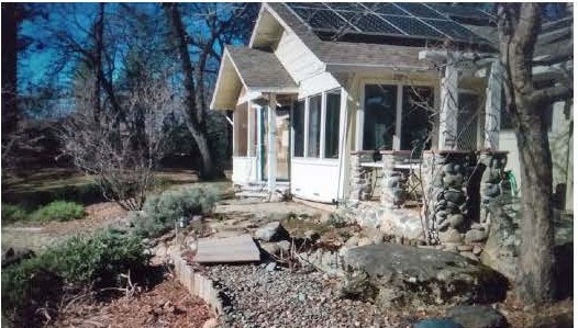 A house with large windows, surrounded by trees and a rocky pathway in the garden.