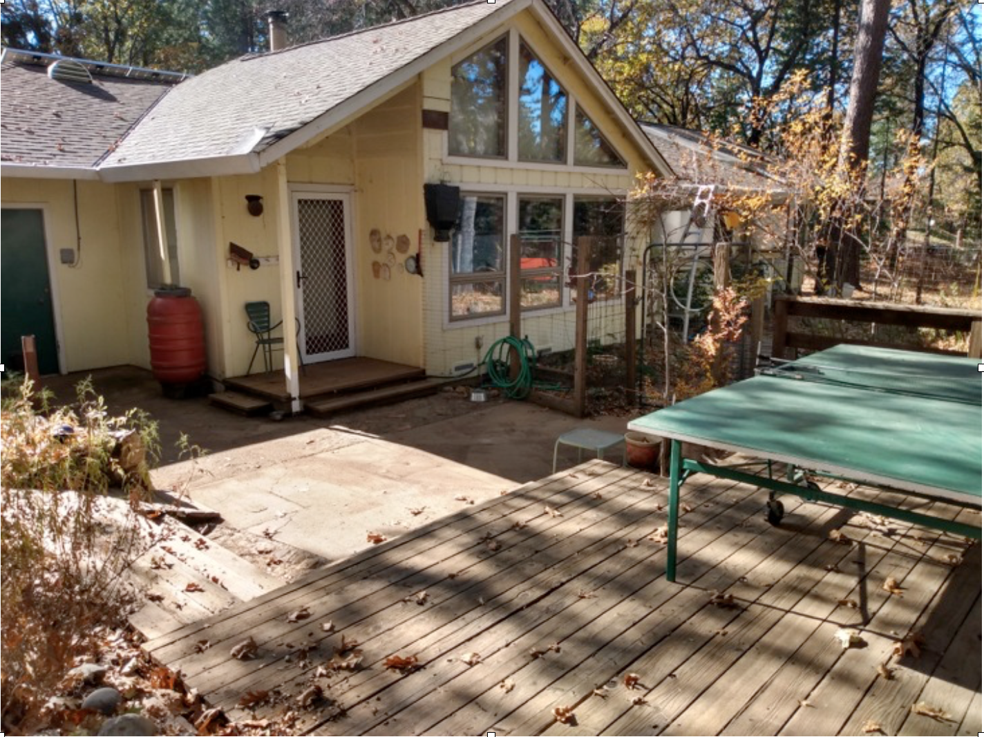 A backyard with a ping pong table, deck, chairs, house with large windows, and scattered autumn leaves.