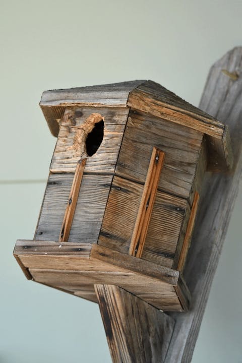 A weathered wooden birdhouse attached to a post.